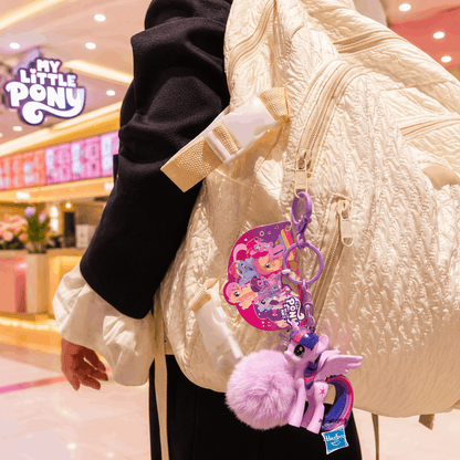 Person wearing a cream jacket with a colorful keychain featuring 'My Little Pony' characters in a mall setting.