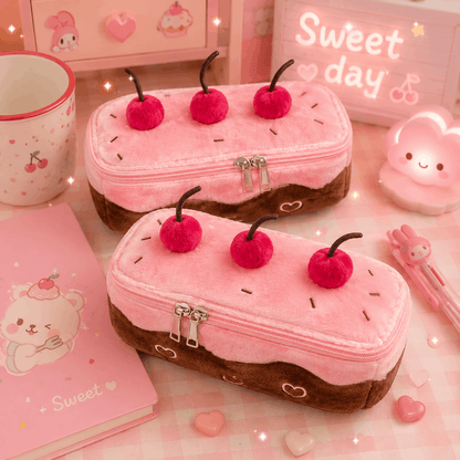 Two pink and brown pencil cases resembling cake slices with cherry toppings on a pink surface.