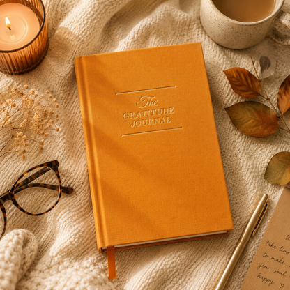 Orange gratitude journal on a textured surface with a candle, glasses, and pen.