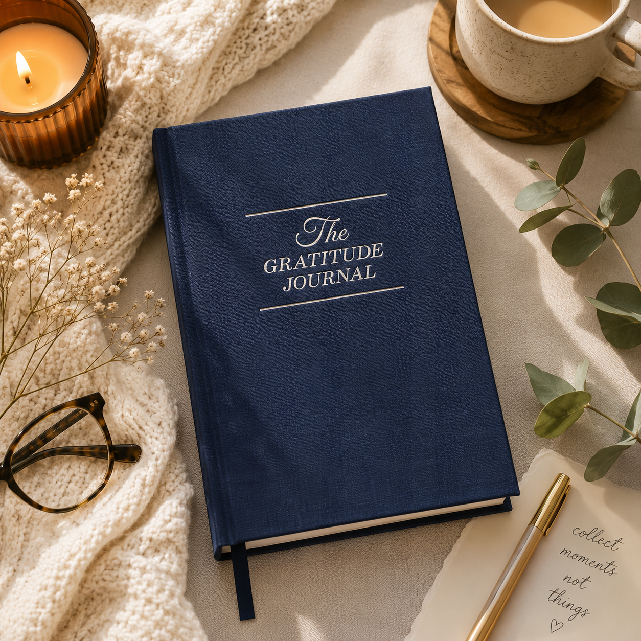 Blue gratitude journal on a table with a candle, glasses, and pen.