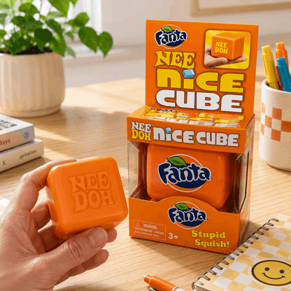 Orange Fanta Nee Doh Nice Cube toy held by a hand on a wooden surface with packaging in the background.