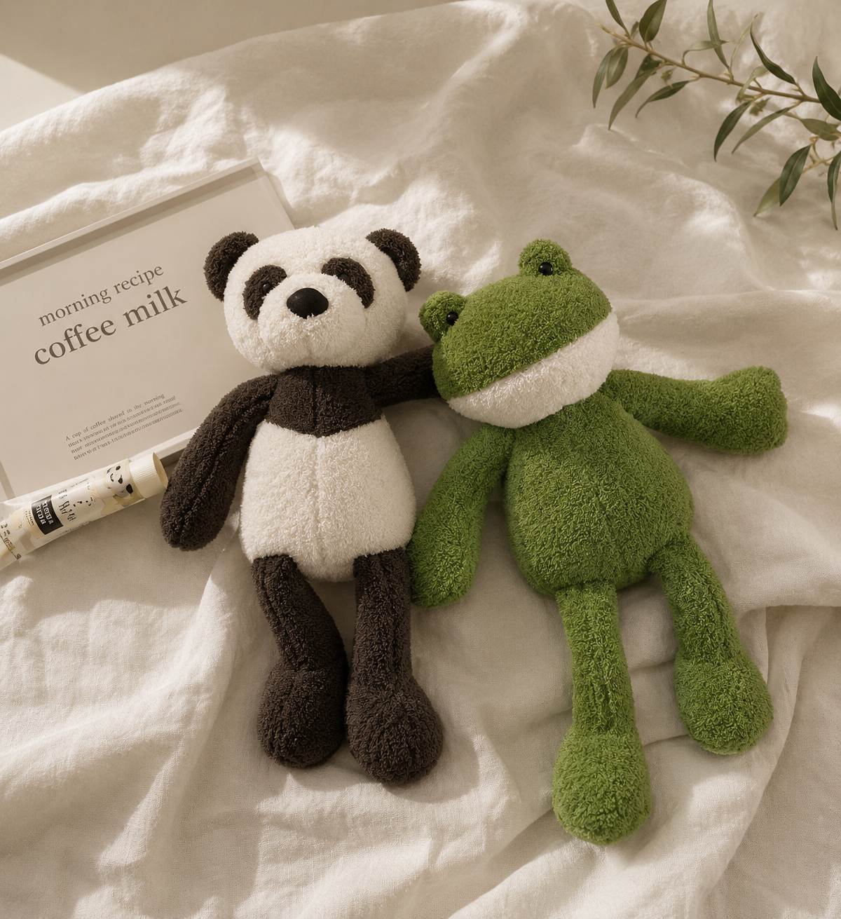 Plush panda and frog toys on a textured surface with a magazine and plant in the background.