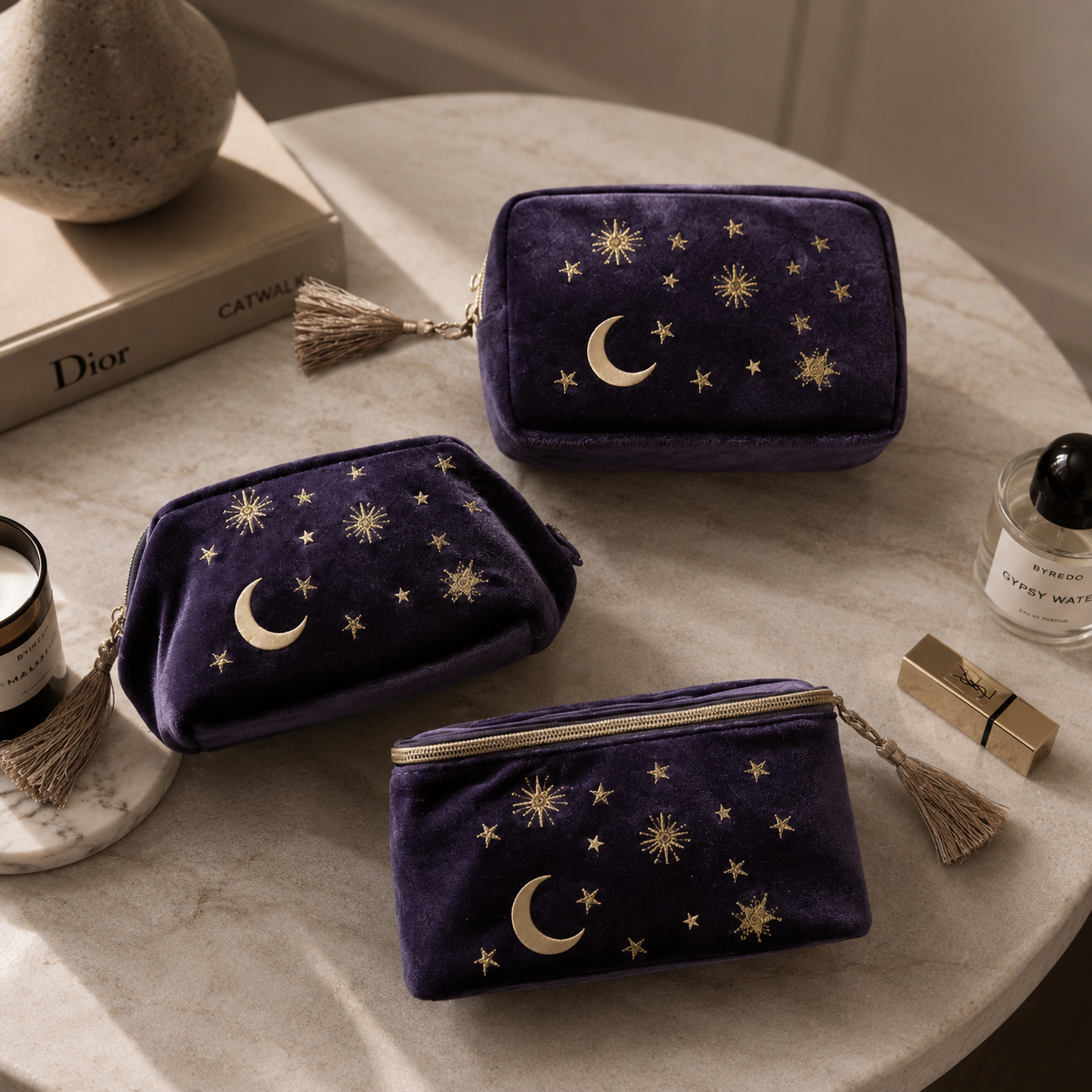 Three purple velvet pouches with star and moon designs on a table with cosmetic items.