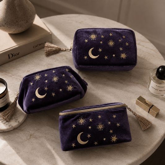 Three purple velvet pouches with star and moon designs on a table with cosmetic items.