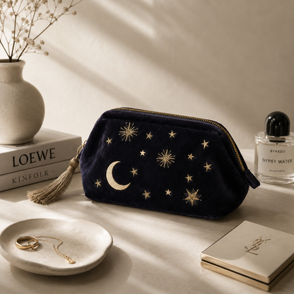 Navy blue pouch with star and moon designs on a surface with books and a bottle of perfume.