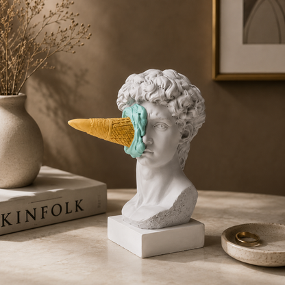 Bust with a carrot and ice cream cone for a head on a table with a book and decorative items.