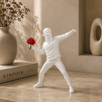 White sculpture of a figure holding red flowers next to a beige vase and 'KINFOLK' book on a wooden surface.