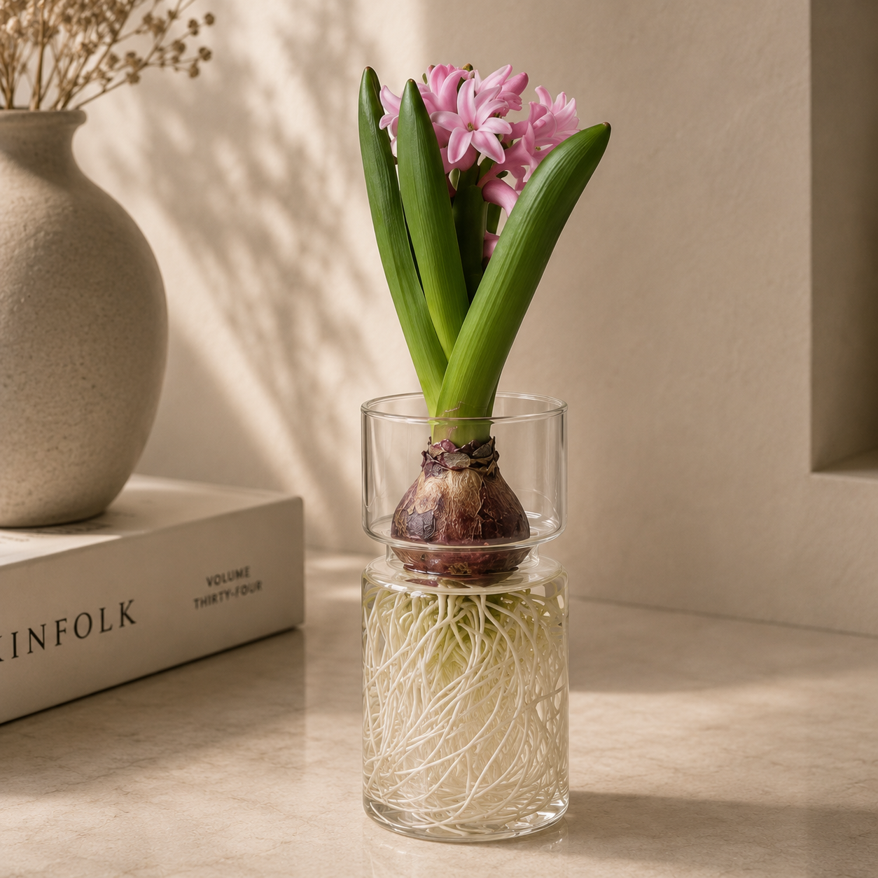 Small glass vase with a growing plant and pink flowers on a wooden surface.