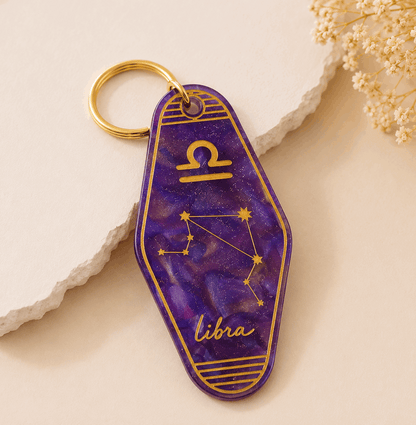 Purple keychain with Libra zodiac design on a light beige background