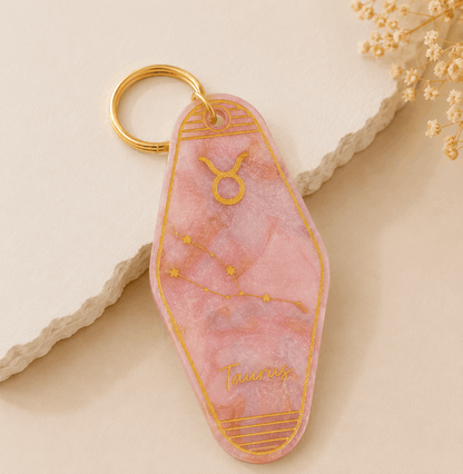 Pink keychain with gold accents on a beige surface