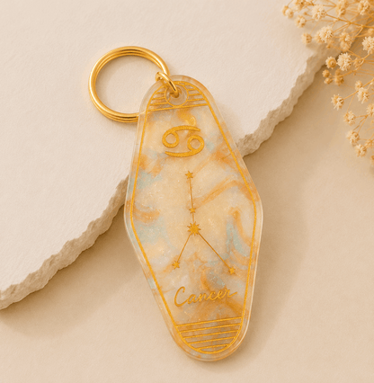 Keychain with Cancer zodiac design on a beige stone surface with dried flowers.
