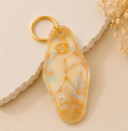 Keychain with Cancer zodiac design on a beige stone surface with dried flowers.