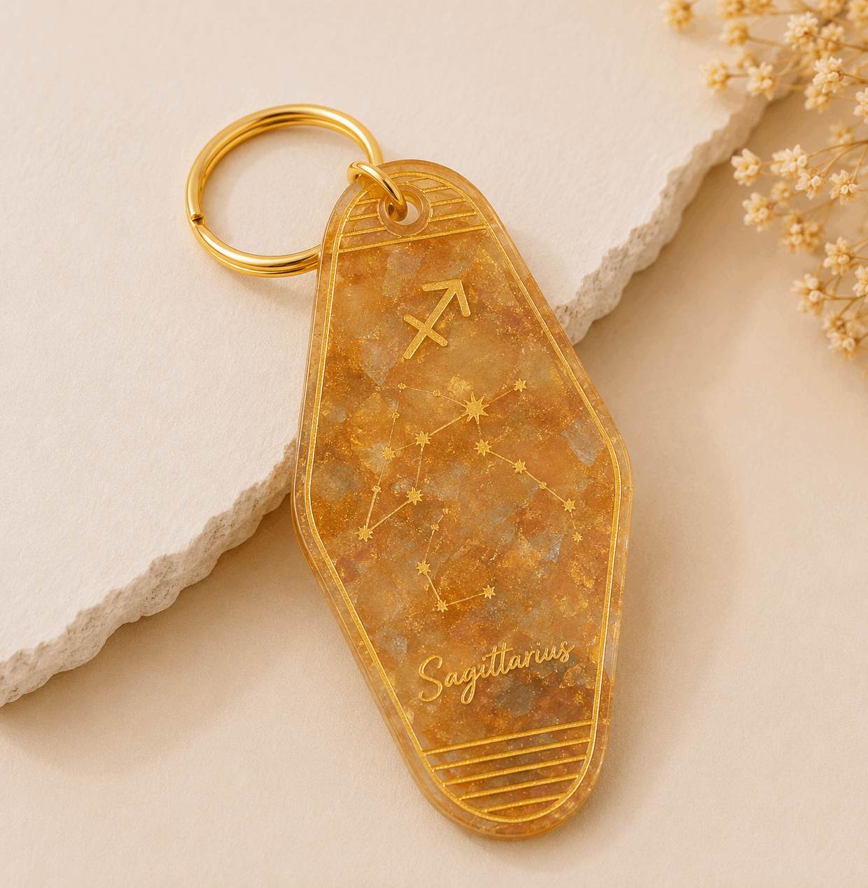 Gold keychain with Sagittarius constellation design on a beige surface