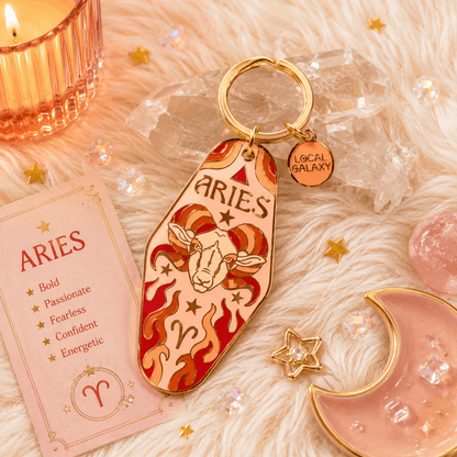 Keychain with Aries design on a soft fabric background with decorative items.