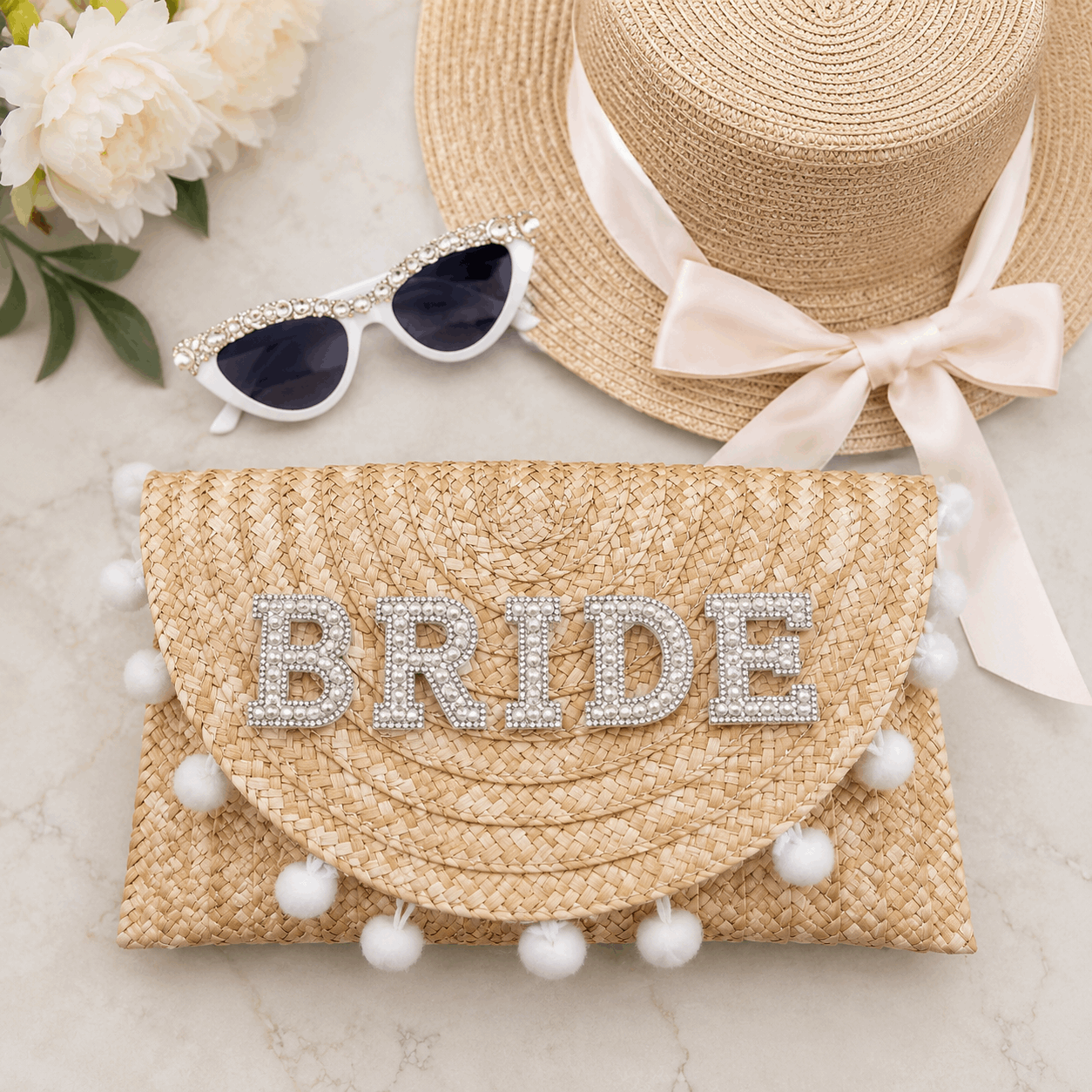 Straw clutch with 'BRIDE' embellishments, sun hat, and sunglasses on a light background
