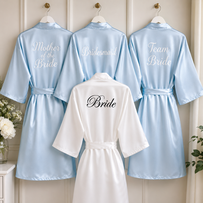 Set of satin robes with embroidered text on a wooden background