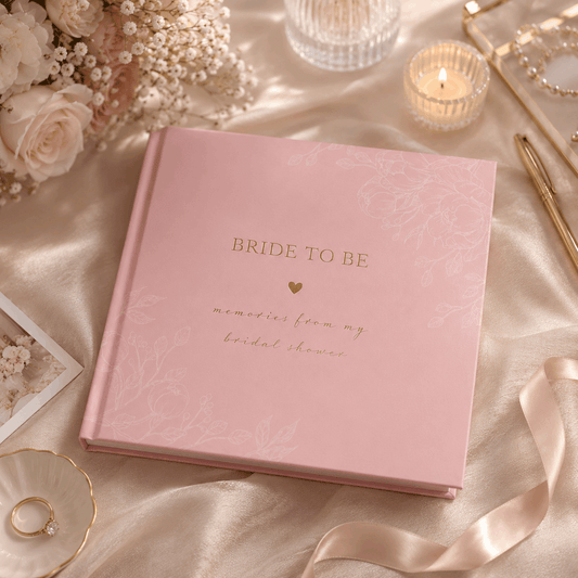 Pink 'Bride to Be' memory book on a decorative table with flowers and candles.