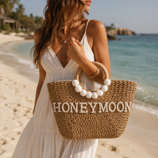 Woman holding a straw bag with 'Honeymoon' text on a beach