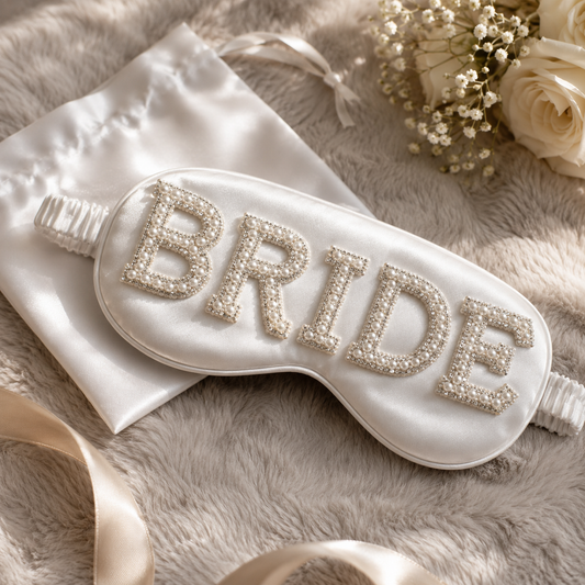 Sleep mask with 'BRIDE' embroidery on a soft surface with flowers and ribbons.