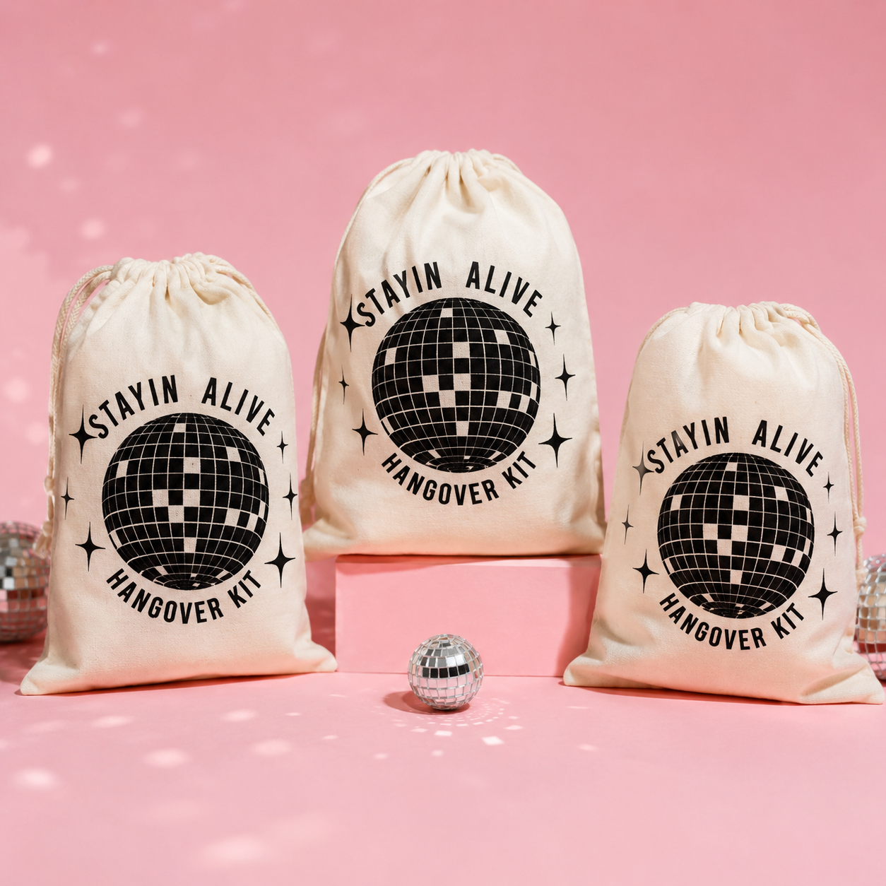 Three 'Stayin Alive Hangover Kit' bags with a disco ball design on a pink background.