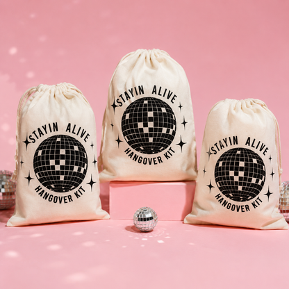 Three 'Stayin Alive Hangover Kit' bags with a disco ball design on a pink background.