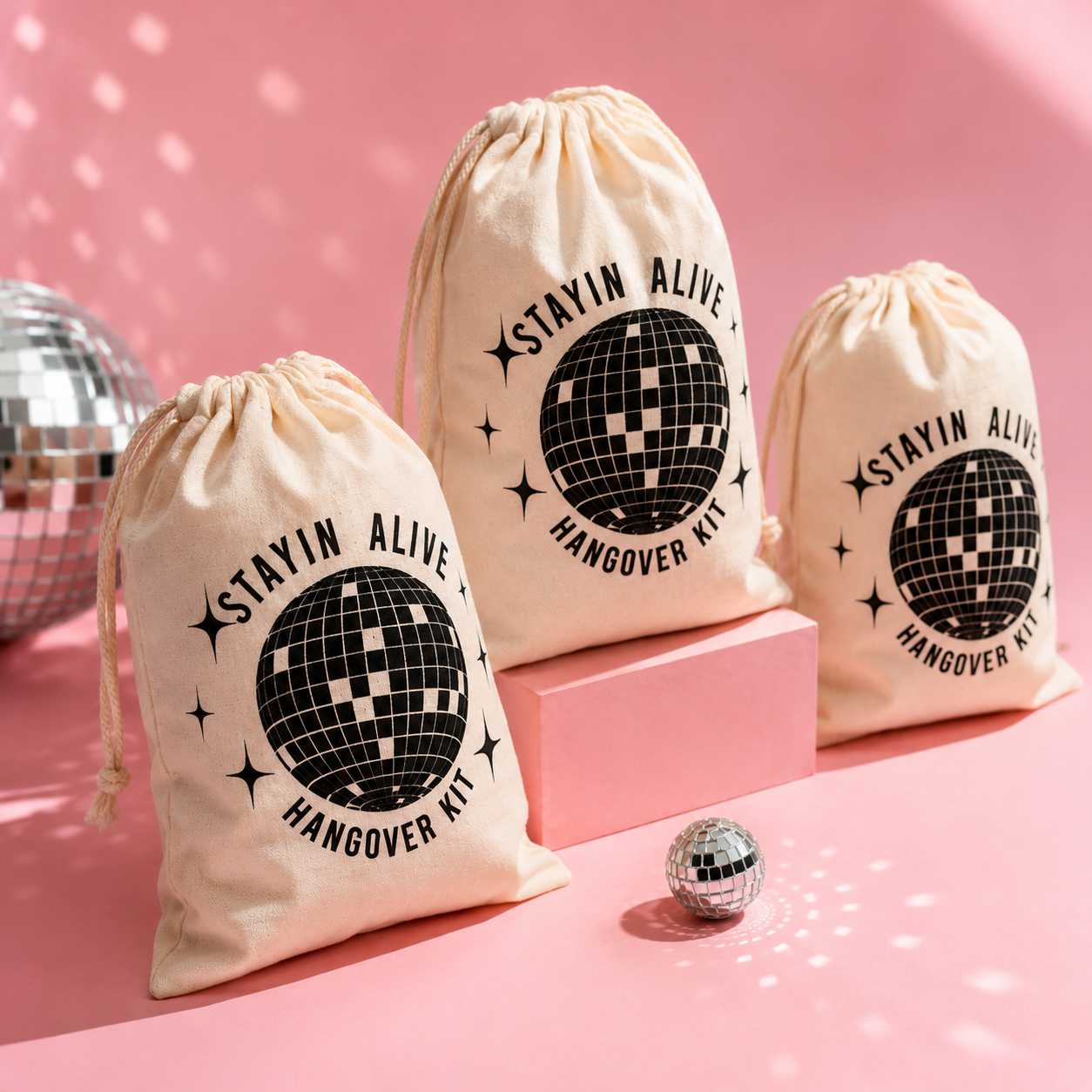 Three 'Stayin Alive Hangover Kit' bags with disco ball design on a pink background