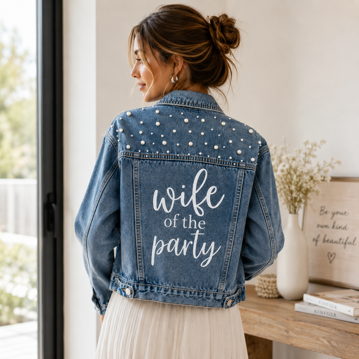 Woman wearing a denim jacket with 'wife of the party' text in a home setting