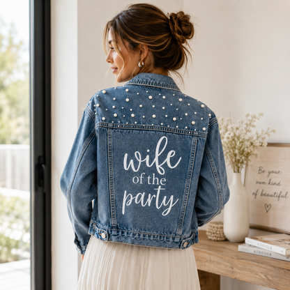 Woman wearing a denim jacket with 'wife of the party' text in a home setting