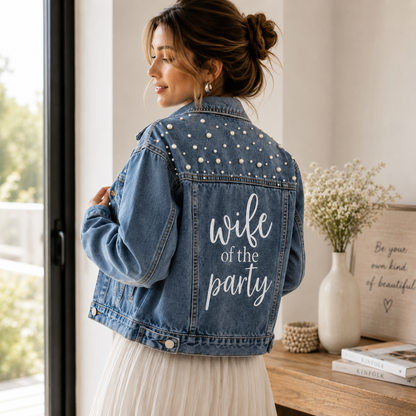Woman wearing a denim jacket with 'wife of the party' text, standing in a bright room.