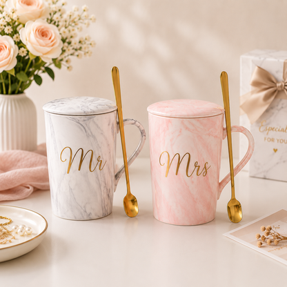 Two marble-patterned mugs labeled 'Mr' and 'Mrs' with gold spoons on a decorative table.
