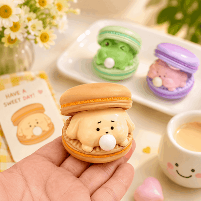 Kawaii-style macaron with a bear face held by a hand, with more macarons and a card in the background.