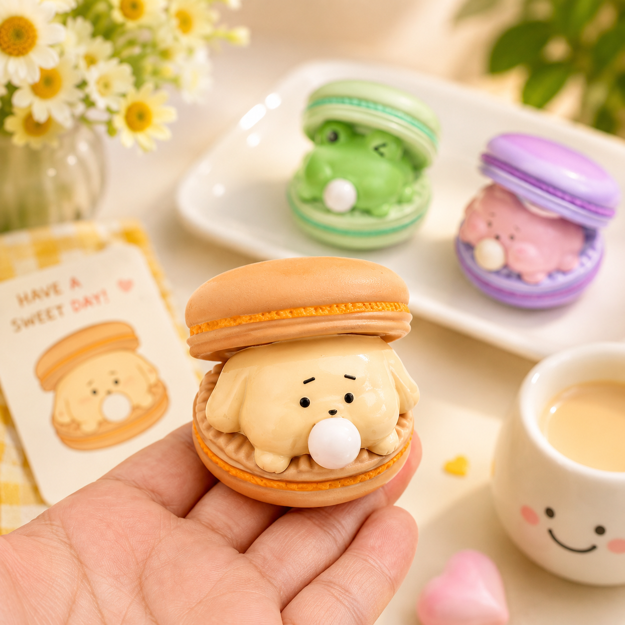 Kawaii-style macaron with a bear face held by a hand, with more macarons and a card in the background.
