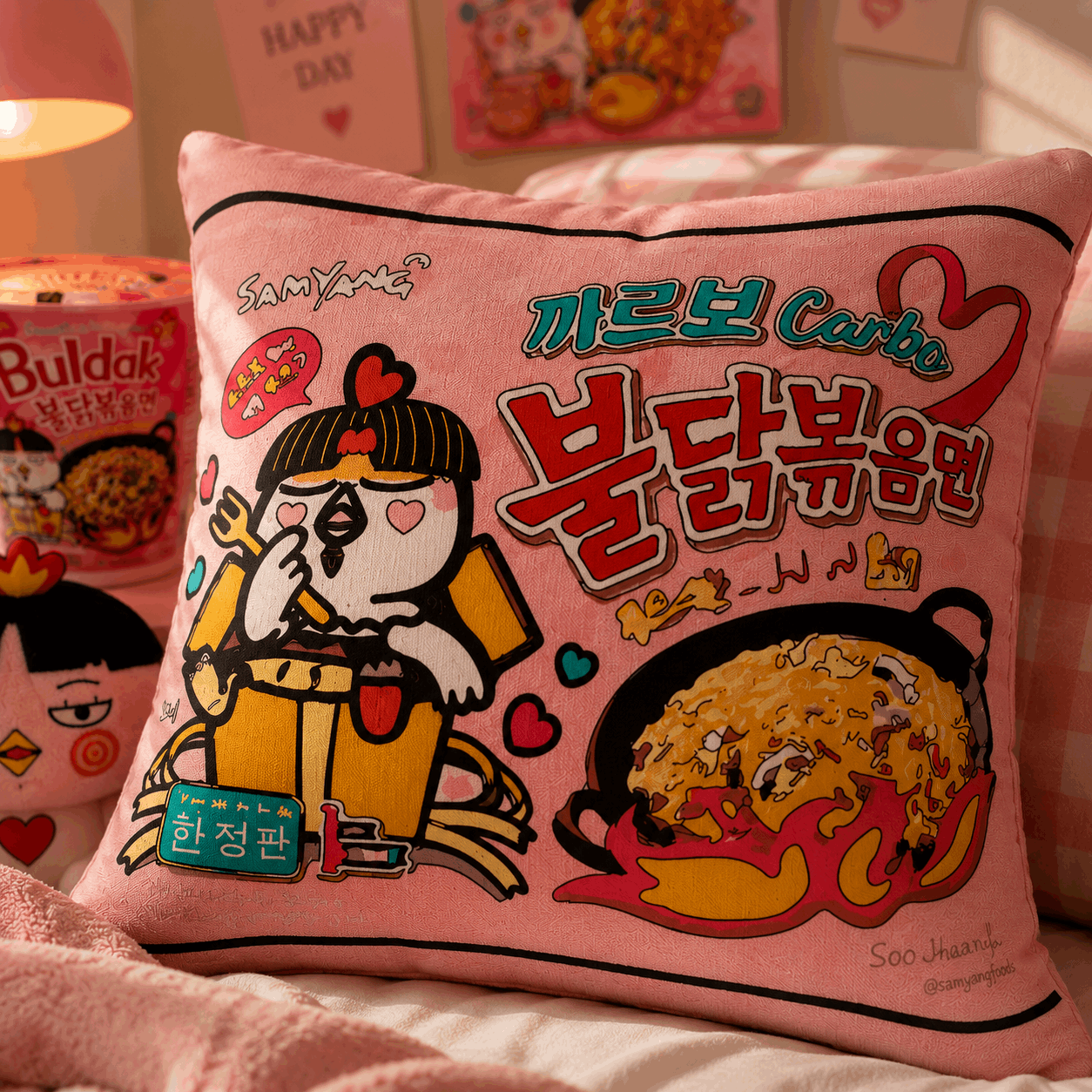 Pink pillow with cartoon character and Korean text on a bed with snacks in the background