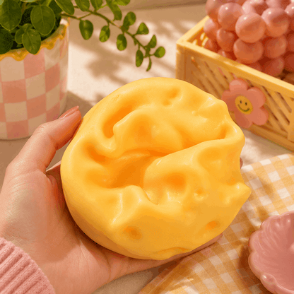 Hand holding a yellow cat-shaped sponge with a checkered tablecloth and decorative items in the background