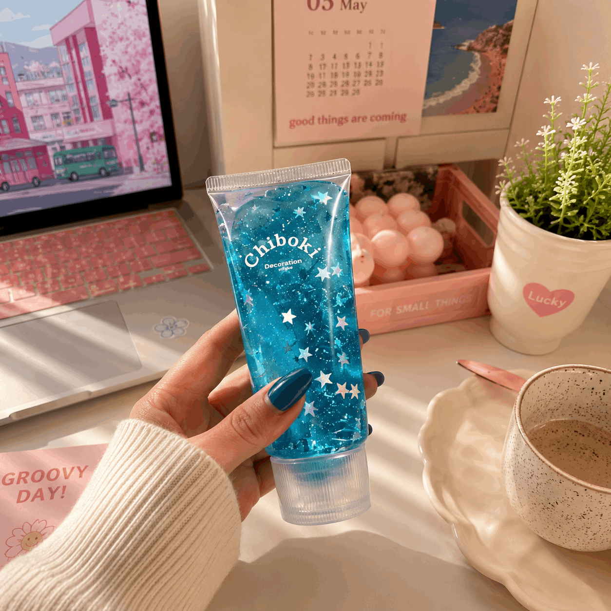 Hand holding a blue Chiboki product on a desk with a laptop, calendar, and plant in the background.