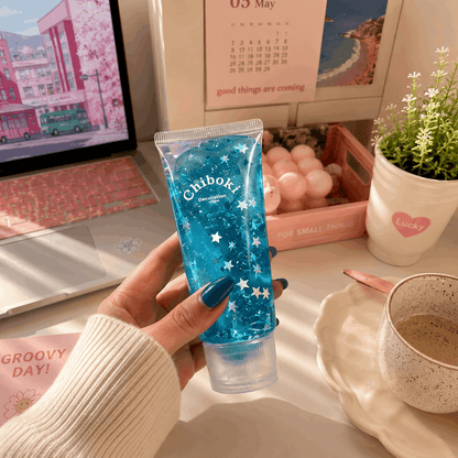 Hand holding a blue Chiboki product on a desk with a laptop, calendar, and plant in the background.