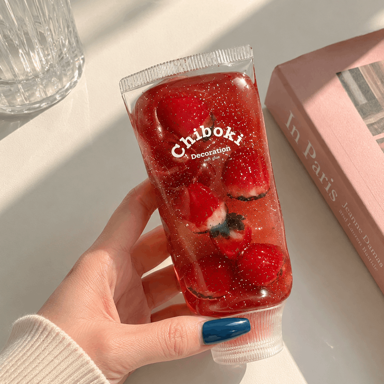 Hand holding a clear container with red gummy bears labeled 'Chiboki' on a light surface.