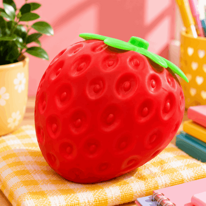 Red strawberry-shaped container on a yellow checkered tablecloth with a pink wall in the background.