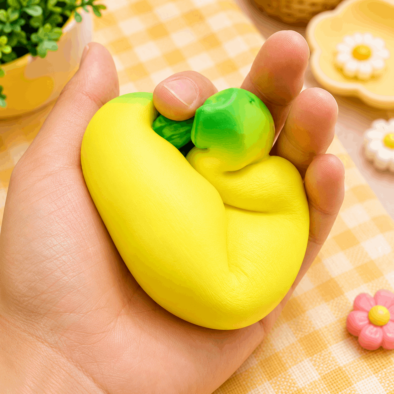 Hand holding a yellow and green stress ball with a checkered tablecloth in the background