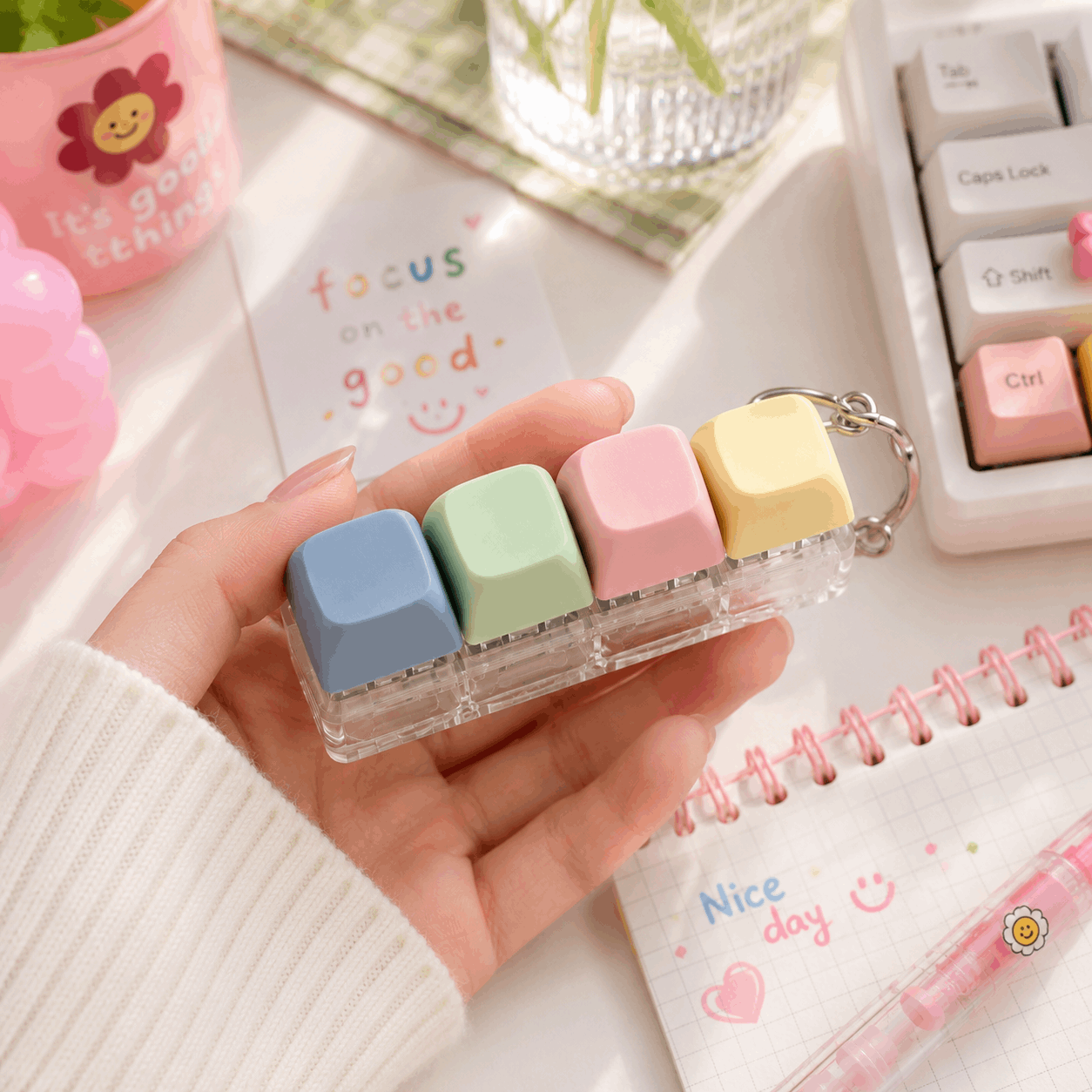 Hand holding a small transparent case with colorful square objects, surrounded by stationery items on a desk.