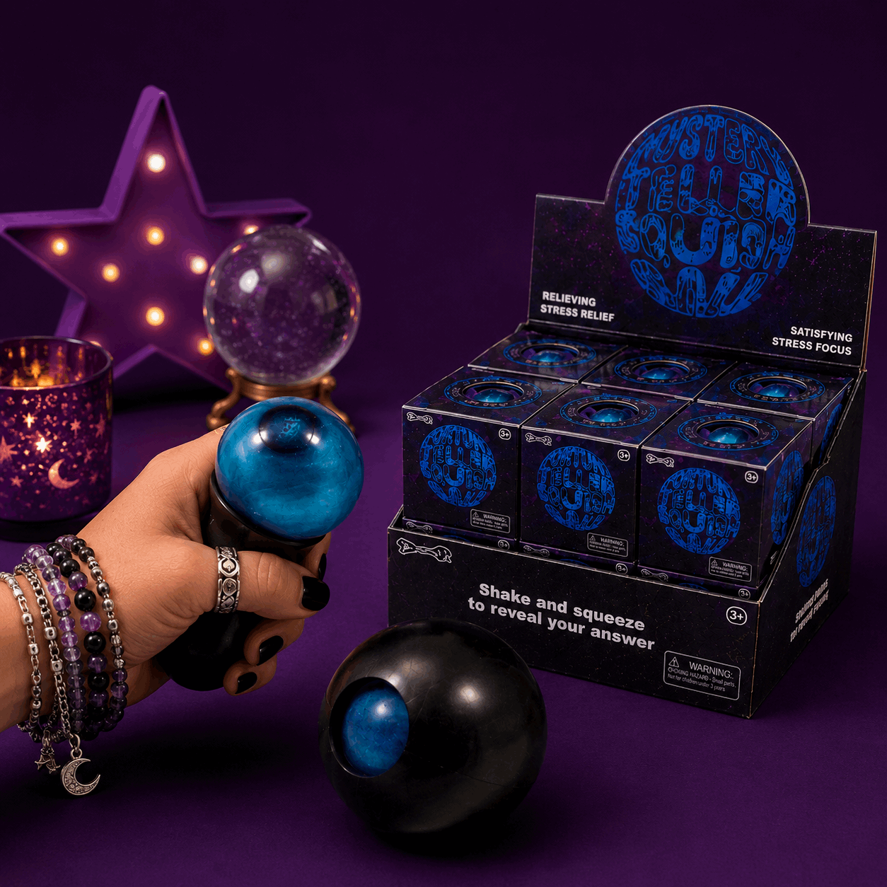 Hand holding a blue stress ball with a box of similar balls in the background on a purple surface.