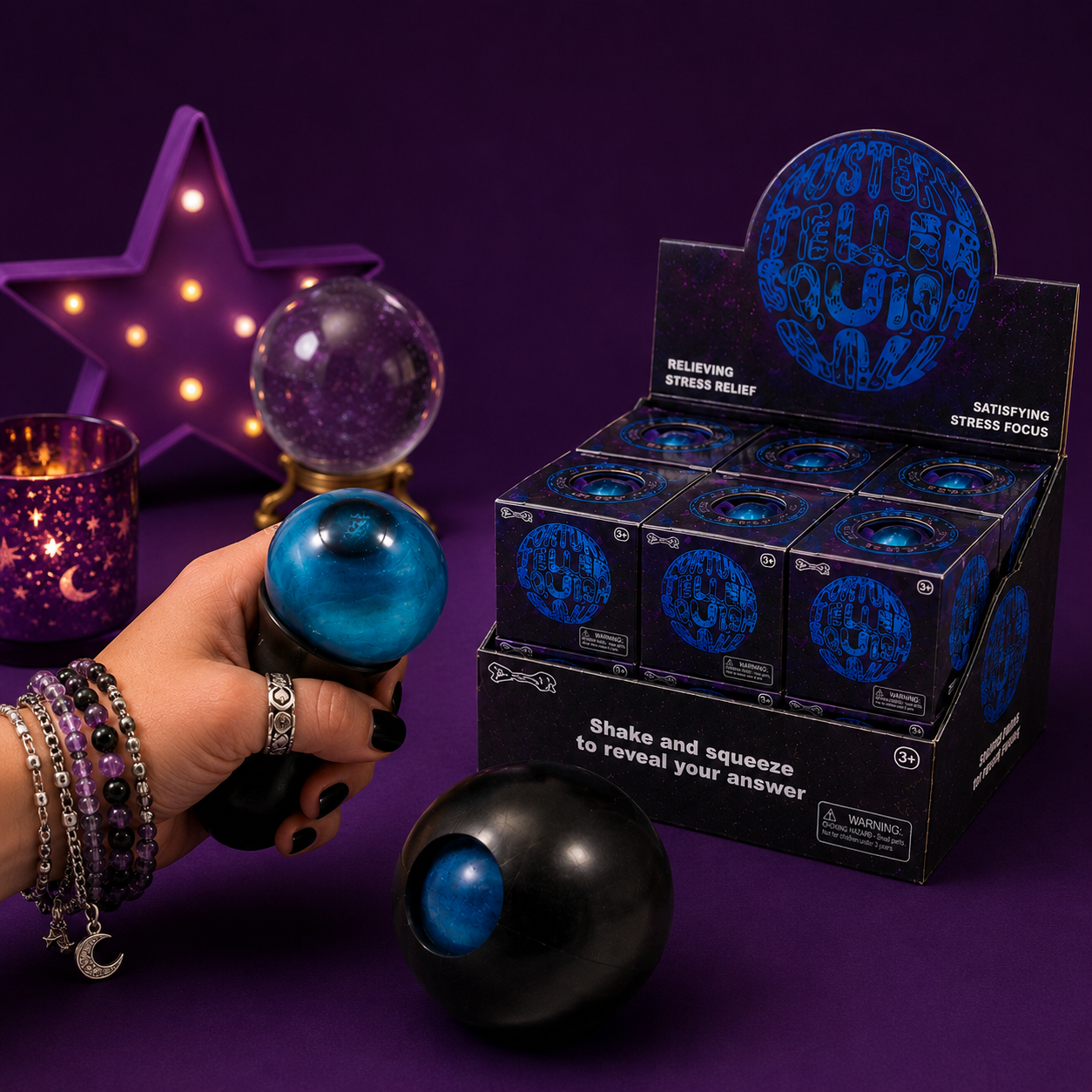 Hand holding a blue stress ball with a box of similar balls in the background on a purple surface.