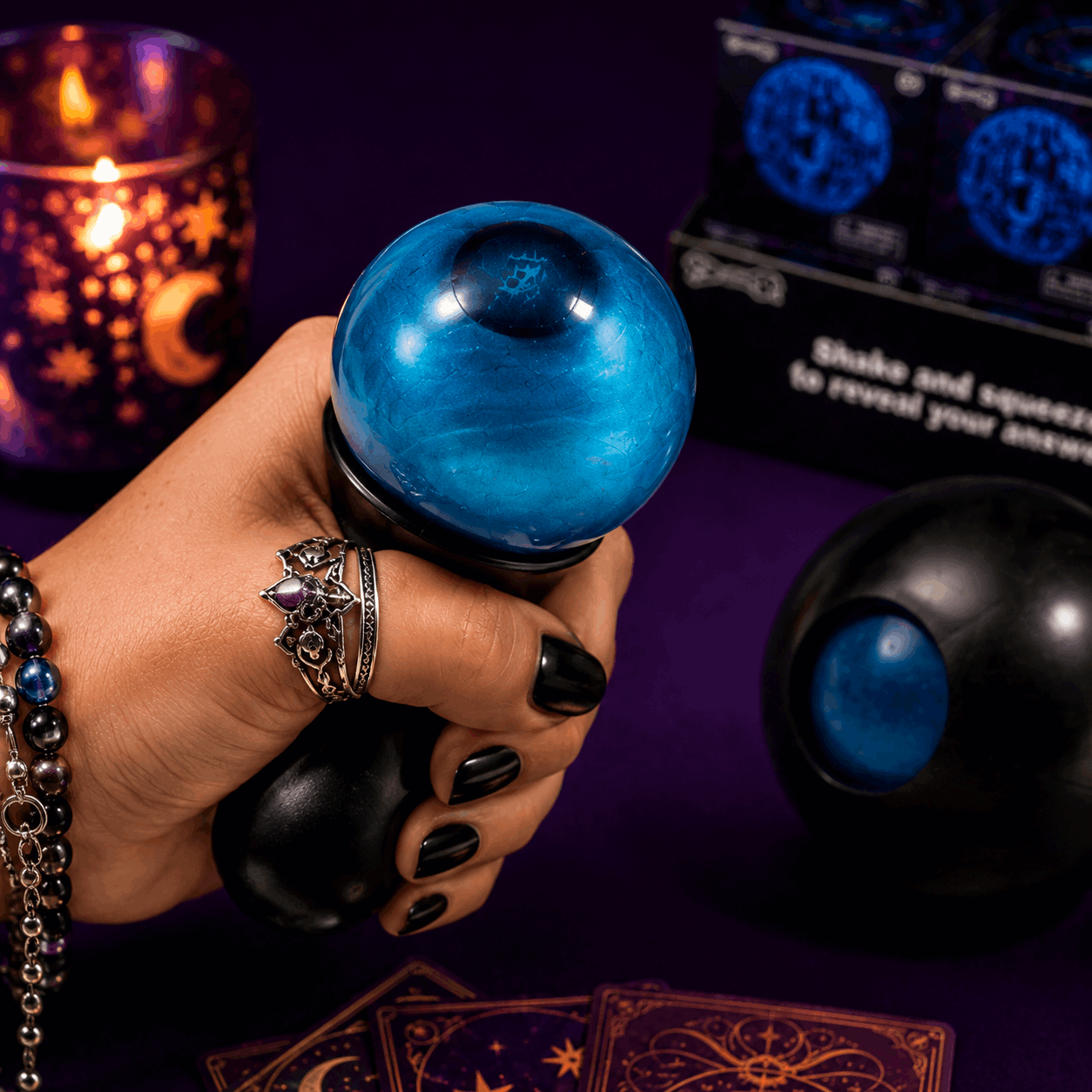 Hand holding a blue crystal ball with tarot cards and candles in the background