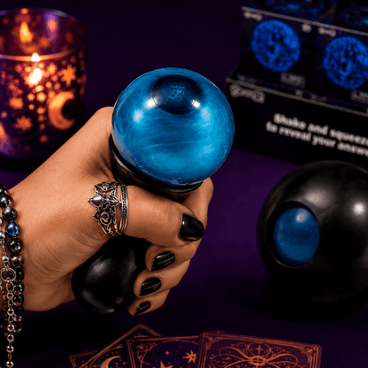 Hand holding a blue crystal ball with tarot cards and candles in the background
