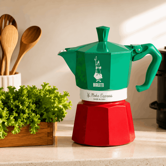 Green and red Bialetti Moka Express coffee maker on a kitchen counter with plants and utensils.