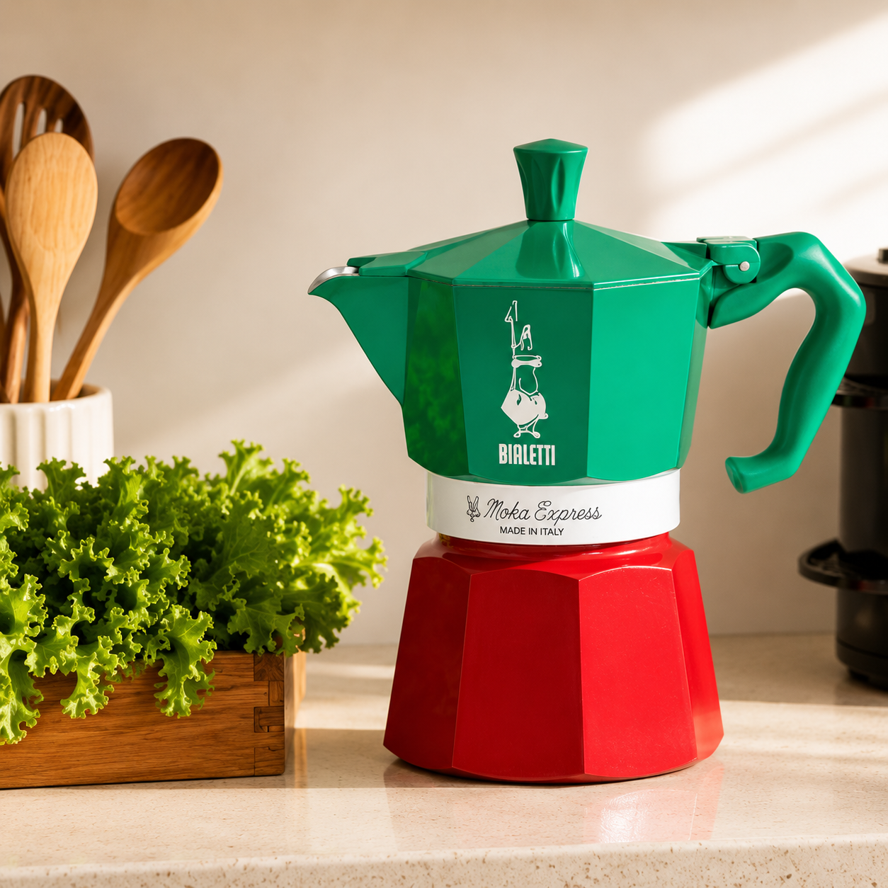 Green and red Bialetti Moka Express coffee maker on a kitchen counter with plants and utensils.