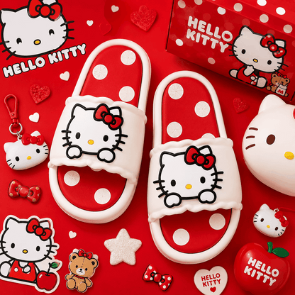 A pair of Hello Kitty slide sandals with white straps, red bows, and red-and-white polka dot soles, arranged on a red background with Hello Kitty-themed accessories and packaging.