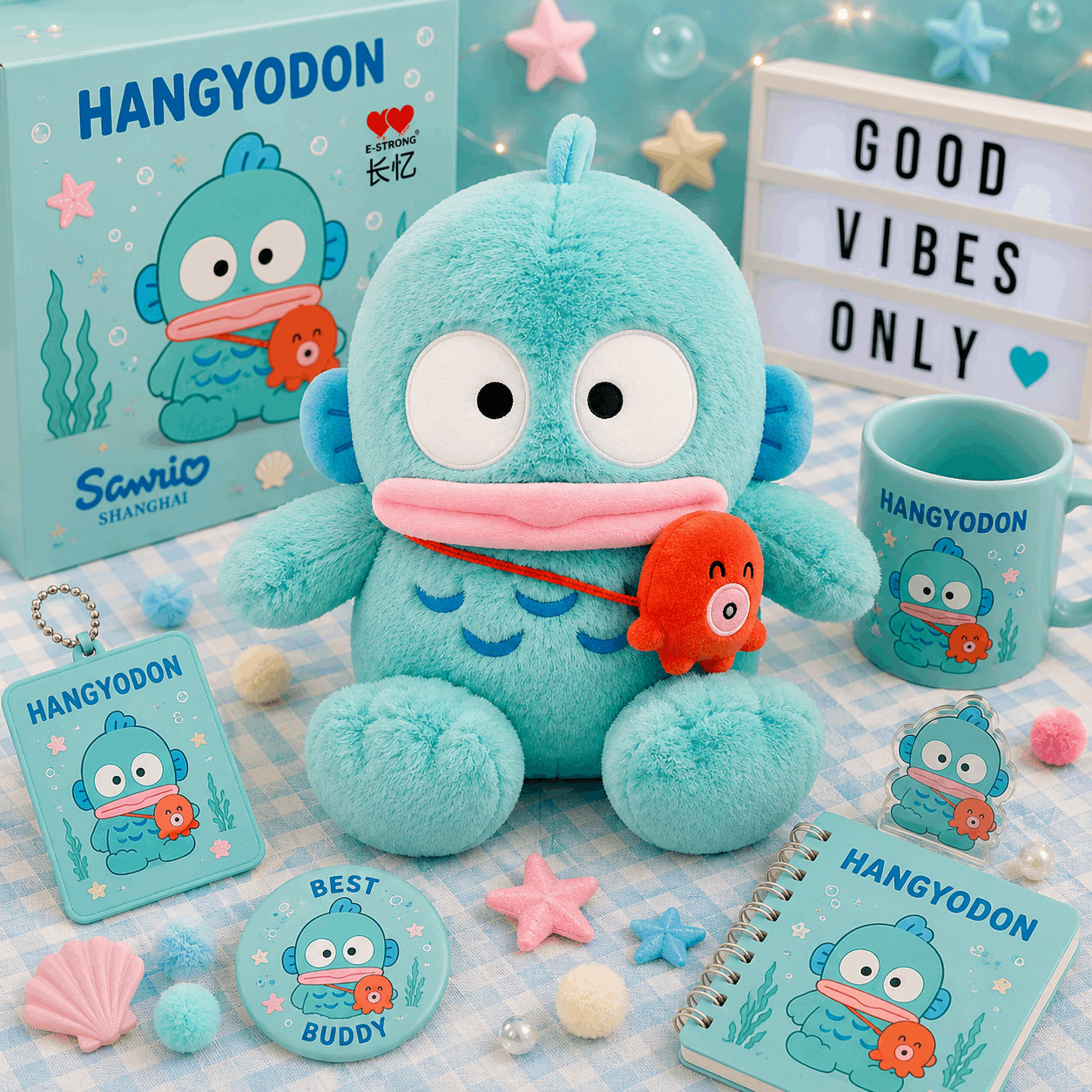A Sanrio Hangyodon merchandise display featuring a plush toy, a mug, a notebook, a card, a pin, and a box, all decorated with the blue Hangyodon character and an orange fish, arranged on a checkered blanket with decorative props.