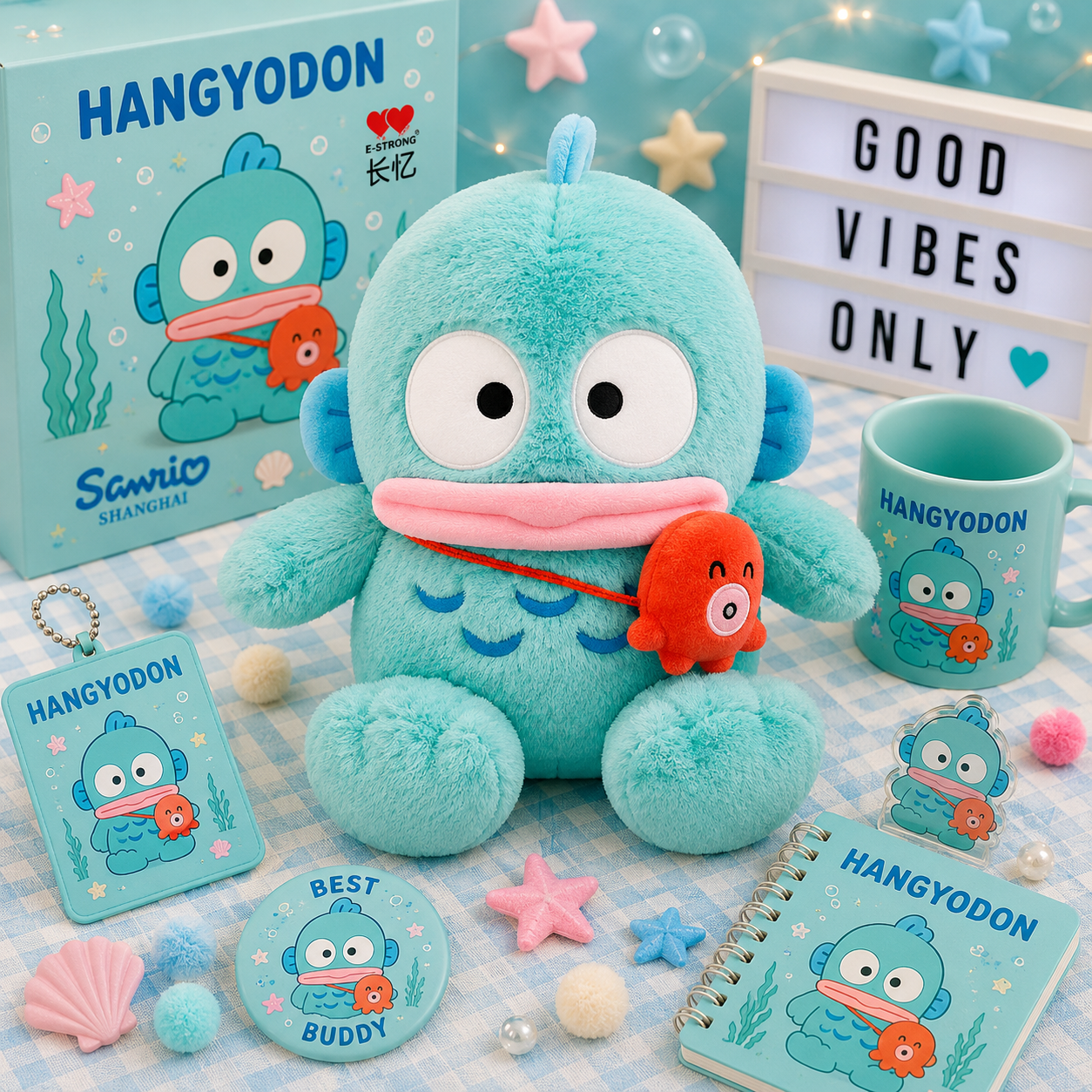 A Sanrio Hangyodon merchandise display featuring a plush toy, a mug, a notebook, a card, a pin, and a box, all decorated with the blue Hangyodon character and an orange fish, arranged on a checkered blanket with decorative props.