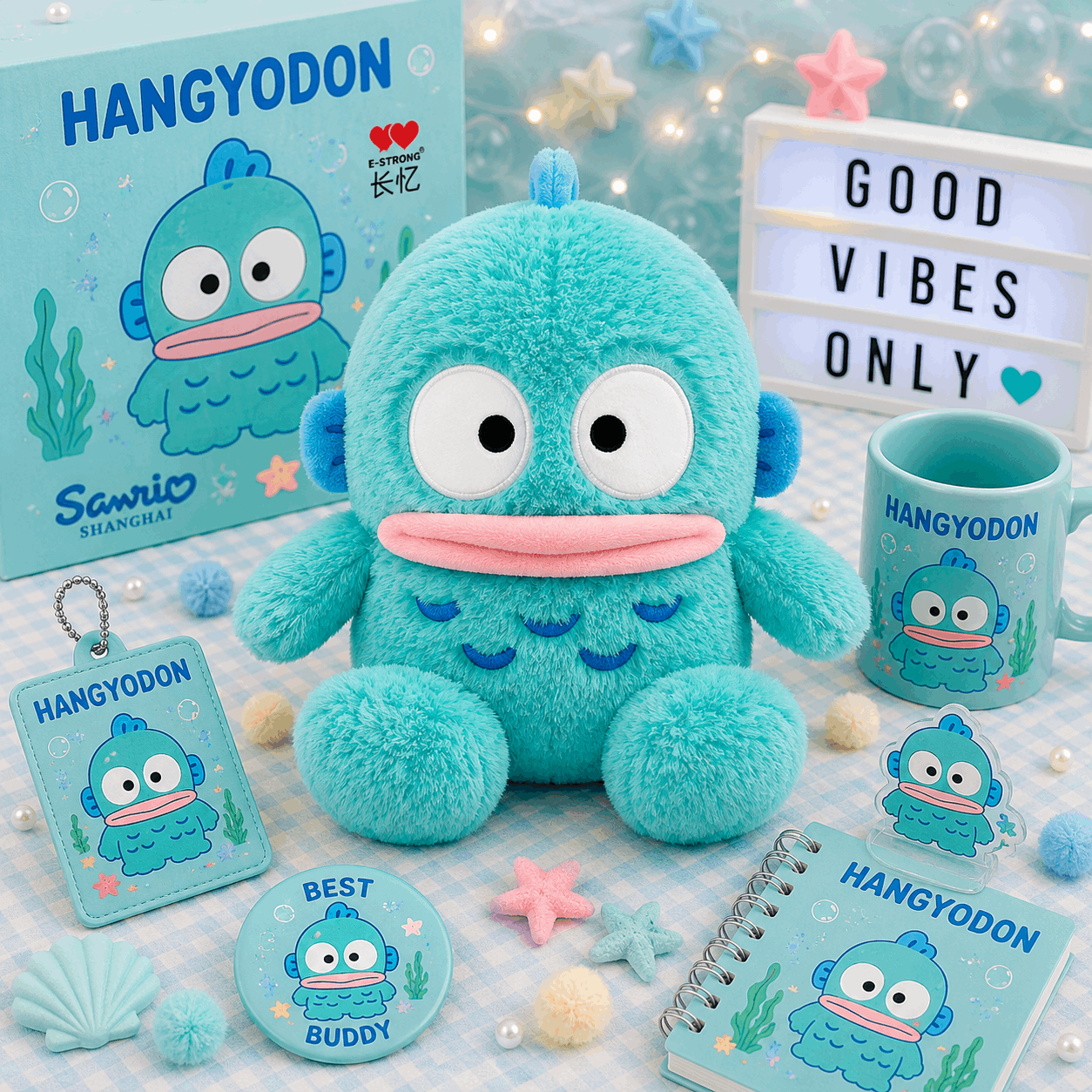 A turquoise cartoon sea monster merchandise set arranged on a pastel blue checkered surface, including a plush toy, box, mug, notebook, card, round sticker, and small accessories. The box and printed items show the brand name Hangyodon and Sanrio Shanghai.
